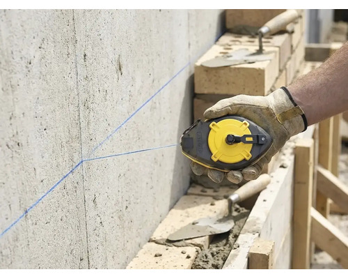Artisan marquant une ligne droite avec un cordeau à tracer sur un mur en béton sur un chantier avec de la maçonnerie.