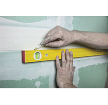 Un niveau à bulle est maintenu contre un mur tandis qu'une personne trace un trait au crayon le long du bord supérieur.