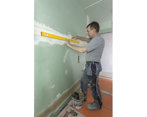 Un artisan utilise un niveau à bulle et un crayon pour tracer une ligne horizontale sur une cloison sèche verte.