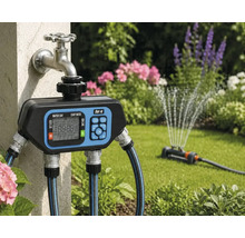 Programmateur d'arrosage numérique for.q sur un robinet extérieur avec tuyaux d'arrosage raccordés et arroseur de pelouse actif dans le jardin.