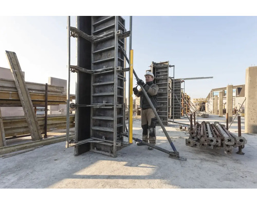 Bauarbeiter richtet eine vertikale Schalung auf einer hellen Baustelle mit einer Wasserwaage und einer Metallstütze aus.