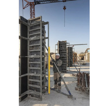 Bauarbeiter prüft die Ausrichtung einer Metallschalung mit einer langen Wasserwaage auf einer Baustelle unter einem Baukran.