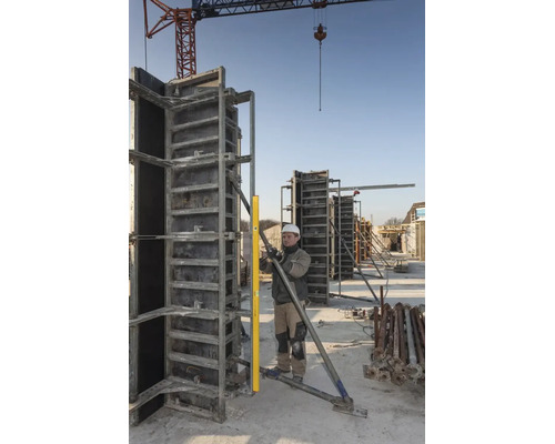 Bauarbeiter prüft die Ausrichtung einer Metallschalung mit einer langen Wasserwaage auf einer Baustelle unter einem Baukran.
