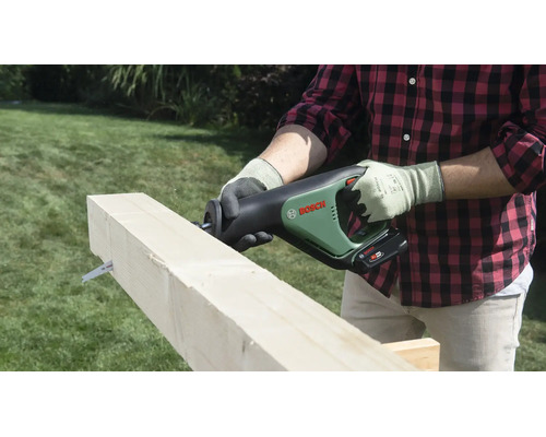 Une personne coupe une poutre en bois avec une scie sabre sans fil Bosch dans un jardin.