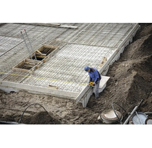 Ouvrier du bâtiment sur un chantier mesurant une fondation en béton avec une armature en acier à l'aide d'un mètre ruban jaune.