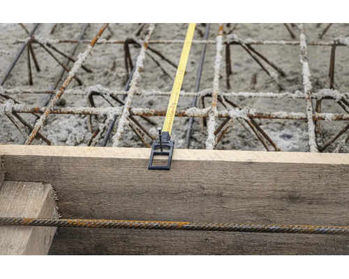 Mètre ruban fixé à un coffrage en bois au-dessus de l'acier d'armature et du béton sur un chantier.