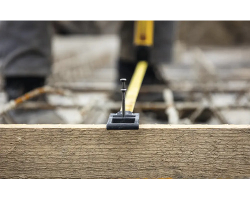 Un mètre ruban accroché à un clou métallique sur une planche en bois pour effectuer une mesure.