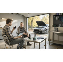 Zwei Männer an enger heller, organiséierter Garage beim Betruechte vun engem Tablet, am Hannergrond en Auto mat oppener Motorhaub an eng Geschierwand.