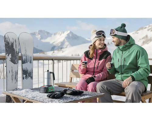 Paar in Wintersportbekleidung sitzt auf einer Holzbank auf einem verschneiten Balkon vor Bergen. Auf dem Tisch steht ein Bosch Akku-Espressokocher.