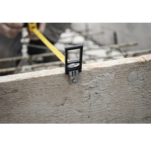 Gros plan d'un mètre ruban accroché au bord d'une planche de bois brute sur un chantier de construction.