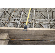 Mètre ruban fixé à un coffrage en bois au-dessus de l'acier d'armature et du béton sur un chantier.
