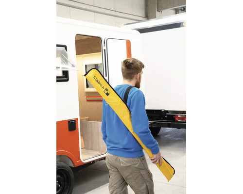 Homme avec un sac de transport Stabila pour niveaux à bulle sur l'épaule à côté d'un véhicule.