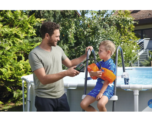 Homme gonflant les brassards d'un enfant avec une pompe à air sans fil près d'une piscine de jardin.