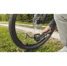 Une main tient une pompe à air sans fil Bosch pour gonfler un pneu de vélo en extérieur.