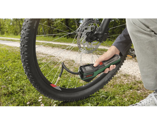 Une main tient une pompe à air sans fil Bosch pour gonfler un pneu de vélo en extérieur.