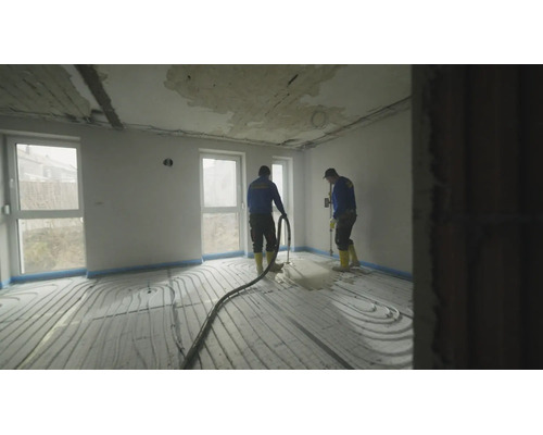 Ouvriers posant une chape liquide sur un chauffage au sol dans une pièce lumineuse lors d'une rénovation.