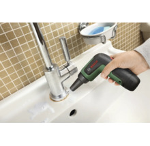 Une main utilise la brosse de nettoyage sans fil Bosch UniversalBrush sur la base d'un robinet de lavabo chromé.