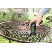 Une personne utilise une brosse de nettoyage Bosch pour enlever la rouille d'une table de jardin ronde en métal.