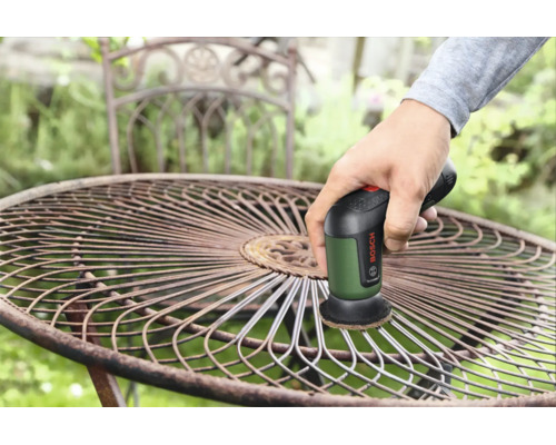 Une personne utilise une brosse de nettoyage Bosch pour enlever la rouille d'une table de jardin ronde en métal.
