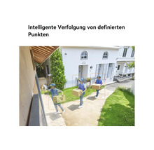 Vue extérieure lumineuse d'une caméra de sécurité montrant le suivi intelligent d'une personne avec un colis devant une maison blanche.