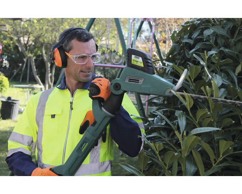 Homme taillant une haie avec un taille-haie motorisé, portant protection auditive, lunettes de sécurité, gants et gilet haute visibilité.