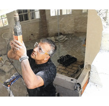 Artisan avec lunettes de protection perçant un plafond en béton avec un perforateur sur un chantier de rénovation.