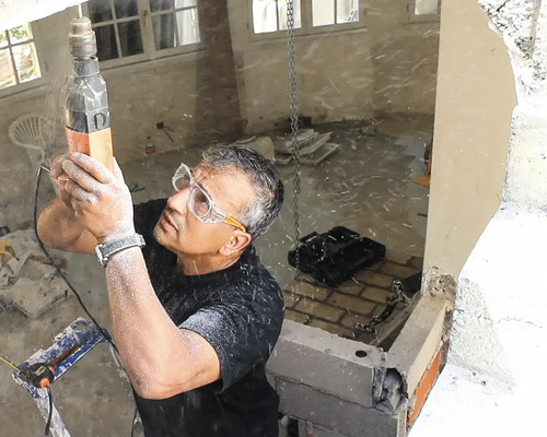 Artisan avec lunettes de protection perçant un plafond en béton avec un perforateur sur un chantier de rénovation.