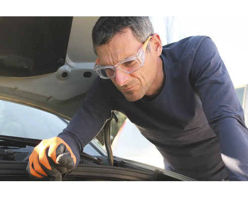 Homme avec lunettes de protection et gants de travail inspectant le moteur sous le capot ouvert d'une voiture.