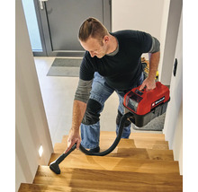 Ein Mann reinigt eine Holztreppe mit einem kompakten Akku-Nass-Trockensauger von Einhell.