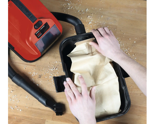 Insertion d'un sac à poussière en papier dans un aspirateur eau et poussière Einhell 18 Volt Power X-Change sur un établi.