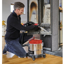 Ein Mann reinigt einen Kaminofen mit einem Einhell Akku-Aschesauger mit Metallbehälter auf Rollen.