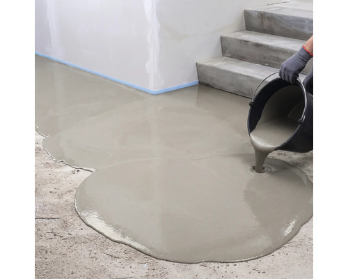 Coulage d'un composé de nivellement liquide à partir d'un seau sur un sol en béton à côté d'un escalier.