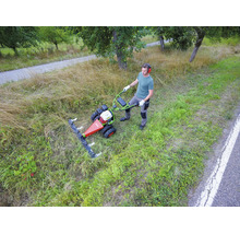 Un homme utilise une motofaucheuse pour couper des herbes hautes dans une prairie en bord de route.