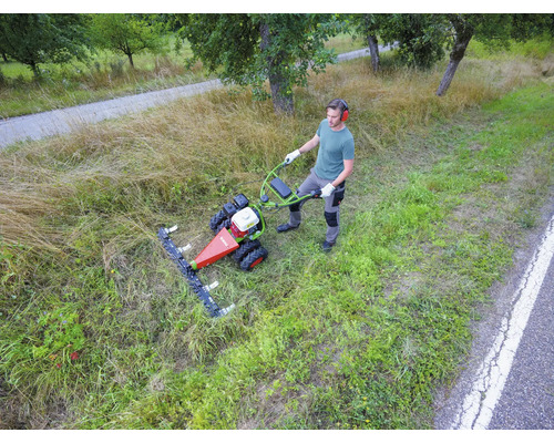 Un homme utilise une motofaucheuse pour couper des herbes hautes dans une prairie en bord de route.