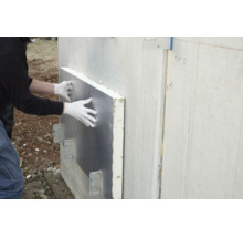 Une personne portant des gants installe un panneau isolant argenté sur un mur extérieur.
