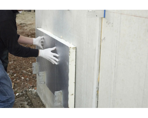 Une personne portant des gants installe un panneau isolant argenté sur un mur extérieur.