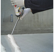 Une personne applique de la mousse polyuréthane sur une plaque avec un pistolet à mousse.