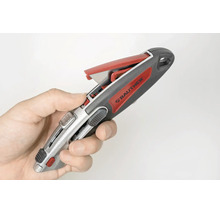Main tenant un cutter Rautner avec un compartiment de rangement pour lames ouvert.