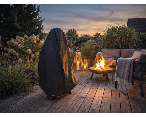 Schwarze Abdeckhaube auf einer Holzterrasse im Garten neben einer Feuerschale und Gartenmöbeln in der Abenddämmerung.