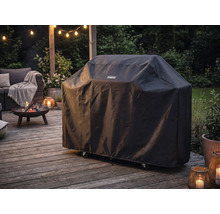 Housse de protection Tenneker pour barbecue sur une terrasse en bois à côté d'un brasero allumé et de meubles de jardin au crépuscule.