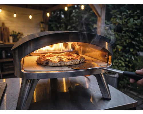 Pizzaofen aus Edelstahl für den Außenbereich mit brennenden Flammen und einer Pizza auf einem Pizzastein, die mit einem Pizzaheber bewegt wird.