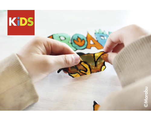 Mains d'enfant décollant un motif de peinture sur vitre avec un dessin de dinosaure. Logo Marabu et Logo KIDS.