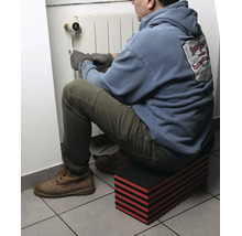 Homme assis sur un repose-genoux modulaire à rayures rouges et noires travaillant sur un radiateur.
