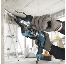 Marteau perforateur Makita perçant du béton sur un chantier lumineux, tenu par une personne avec des gants de travail.