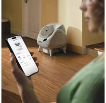Eine Person steuert eine selbstreinigende Catlink Katzentoilette über eine App auf einem Smartphone in einem hellen Raum.