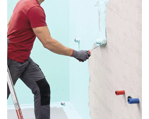 Eine Person trägt mit einer Farbwalze eine Flüssigabdichtung auf eine Wand auf.