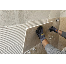 Pose d un grand carreau de mur sur de la colle, mains avec gants de travail et PCI Logo tenant le carreau contre le mur.