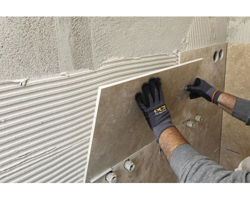 Pose d un grand carreau de mur sur de la colle, mains avec gants de travail et PCI Logo tenant le carreau contre le mur.