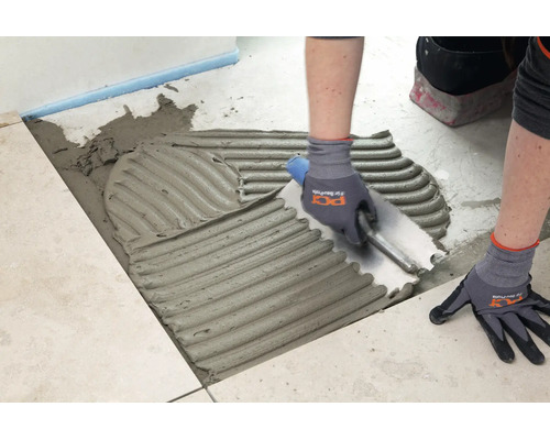Application de colle à carrelage sur le sol à l'aide d'une spatule crantée pour la pose de carreaux de sol.