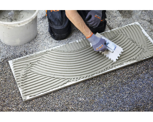 Application de colle à carrelage sur un carreau à l'aide d'une truelle dentelée.
